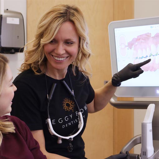 A dentist at a DSD Clinic sits with a patient in a treatment room and shows her a scan of her teeth on the screen of an intraoral scanner.
